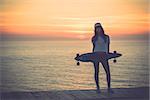 Beautiful and fashion young woman posing at teh sunset with a skateboard - File a little bit noisy