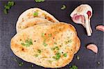 Naan bread with fresh parsley herb and garlic on black background top view. Culinary indian and eastern cuisine.
