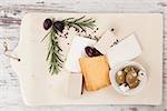 Various cheese, tofu and olives on vintage kitchen board on white wooden textured background top view. Culinary cheese and olives eating, french country style starter.