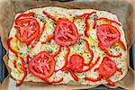 Delicious fresh traditional Italian focaccia bread with tomatoes, red peppers, onions, basil and olive oil on pan ready to cook