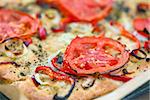 Delicious fresh traditional Italian focaccia bread with tomatoes, red peppers, onions, basil and olive oil on cooking pan