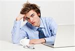 Exhausted young man in the office with the laptop on his front