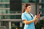 Adult hispanic person with mobile phone and wireless bluetooth headset, talking on telephone in the street out office buildings