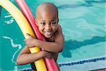 Cute little boy holding foam rollers by the pool at the leisure center