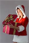 Pretty santa girl opening a gift on gray background