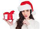 Festive brunette holding gift and keeping a secret on white background