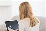 Rear view of a pretty blonde shopping online with laptop at home in the living room