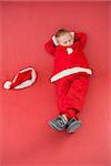 Little boy napping in santa costume on red background