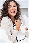 Beautiful young Latina Hispanic woman smiling, laughing, relaxing and drinking a cup of coffee or tea using tablet computer