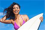 Beautiful young woman surfer girl in bikini with surfboard laughing ready to surf on a beach