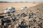 Two off road vehicles driving through a desolate arid rocky desert landscape