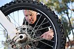 Young male motocross racer adjusting motorcycle wheel in forest