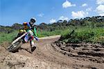 Young male motocross rider racing through mud track bend
