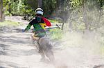 Rear view of young male motocross rider racing on forest track