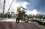 Young male motocross racer jumping mid air down mud hill