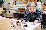 Young craftswoman measuring blueprint on workbench in pipe organ workshop