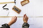 Hands of young craftswoman measuring blueprint in pipe organ workshop