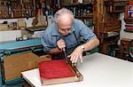 Senior man restoring book in traditional bookbinding workshop