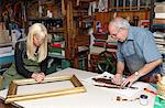 Senior man and young woman restoring picture frame and book spine in traditional bookbinding workshop