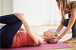 Mature female student lying on back holding knees in pilates class