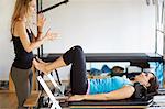 Tutor instructing female student lying on reformer in pilates gym