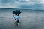 mature woman sitting on deck chair on stormy beach, under umbrella