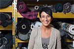 Portrait of mature seamstress in front of rolls of textile in workshop