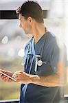 Male doctor holding tablet pc and looking out of hospital window