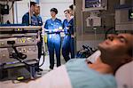 Patient attached to medical monitoring equipment in intensive care unit, doctors standing in doorway