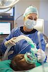 Anesthesiologist holding oxygen mask over patient's face in operating theater