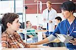 Female doctor holding clip board checking with female patient in outpatient clinic