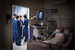 Patient lying in bed in intensive care unit, team of doctors discussing in background