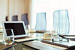 Laptop, eyeglasses and diary on conference table in empty conference room