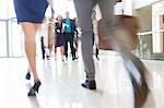 Legs of businesswoman and businessman carrying hand luggage walking through lobby of conference center