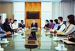 Conference participants looking at man sitting at head of conference table