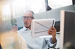 Businessman reading paperwork and cell phone in office