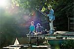 Boy fishing and playing with toy sailboat with father and grandfather at lake