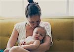 Portrait of mother holding and kissing baby, sitting on sofa by window