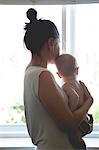 View of mother holding baby and looking through window