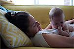 View of mother lying on sofa with little baby sucking thumb