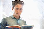 Portrait of university student with book standing beside window