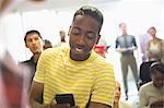 University student texting in classroom, people standing in background