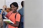 Portrait of smiling university student standing in corridor, people in background looking at exam results