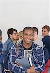 Male student holding books and smiling at camera with other students in background