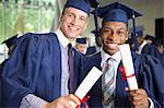 Two laughing male students in graduation clothes holding diplomas