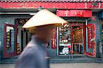 Beijing, China. Old man with conical hat passing in front of a shop in a hutong of Beijing