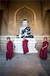 Myanmar, Mandalay division, Bagan. Three novice monks inside a pagoda near a Buddha statue (MR)