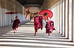 Myanmar, Mandalay division, Bagan. Three novice monks running with red umbrellas in a walkway (MR)