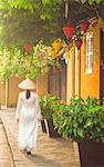 Woman wearing Ao Dai dress walking along street, Hoi An (UNESCO World Heritage Site), Quang Ham, Vietnam (MR)