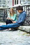 Two students sitting by railings using cell phone and tablet